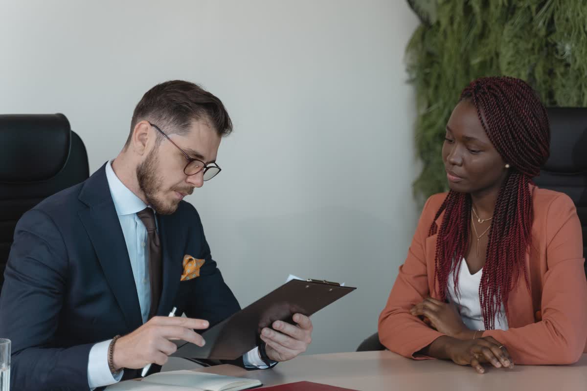 Two people at a table in conversation, one reviewing papers on a clipboard: an illustrative image for a hiring conversation.