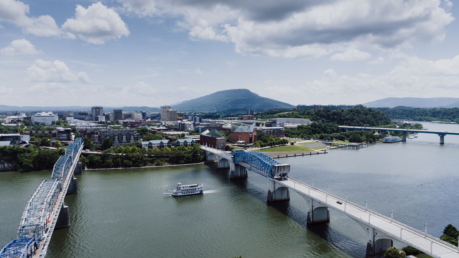 An aerial view of downtown Chattanooga where the Walnut Street and Market Street bridges cross the Tennessee River, Lookout Mountain rising behind.