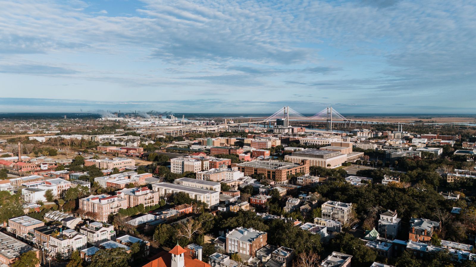 An aerial view over Savannah's historic district toward the Talmadge Memorial Bridge and the port on the horizon.