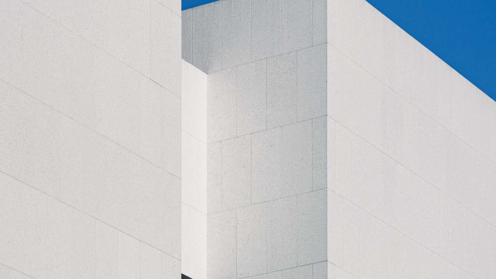 Two white building volumes meeting at a sharp corner against a blue sky, an illustrative image for two disciplines that meet but differ.