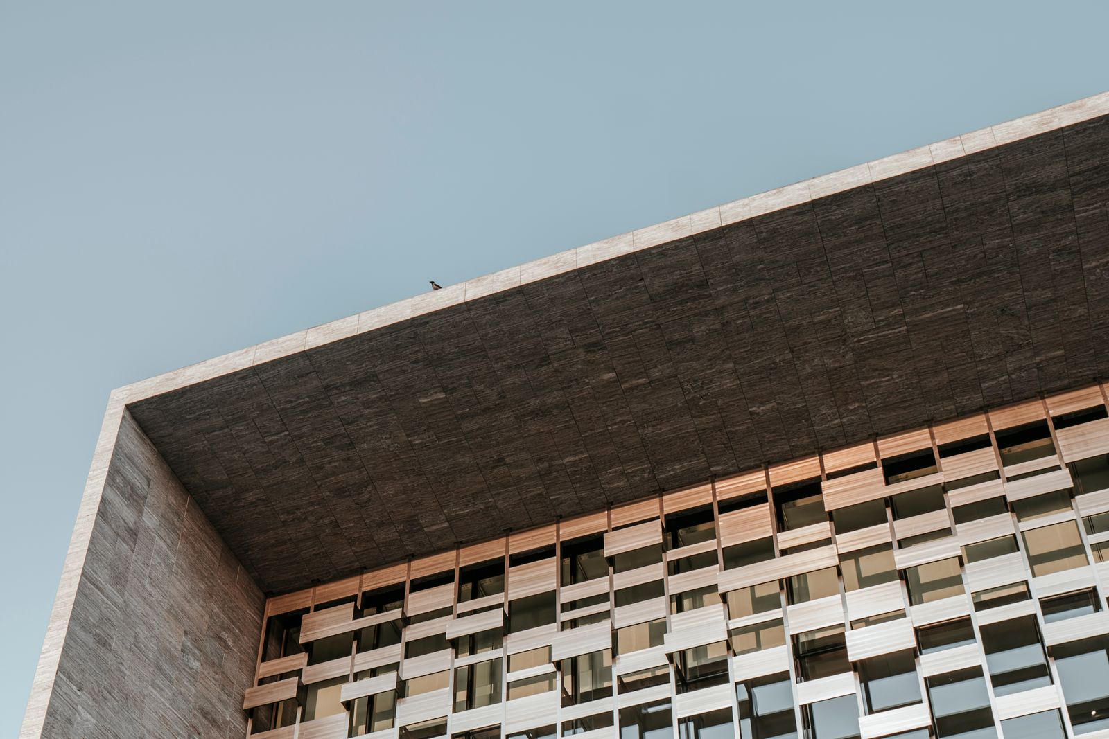 A modern facade of layered panels and glass seen from below, an illustrative image for infrastructure assembled to serve a purpose set elsewhere.