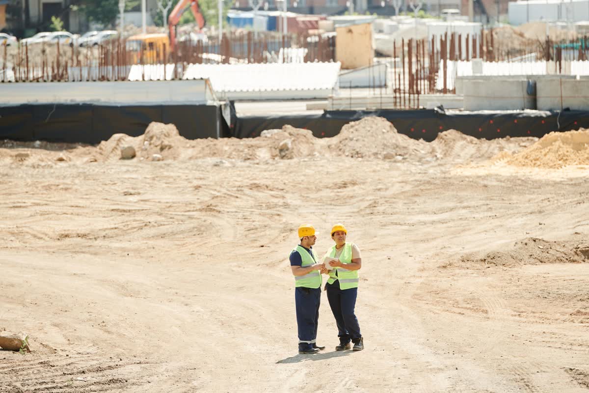 Two workers in hi-vis vests and hard hats standing together on an open construction site: an illustrative image for construction planning.