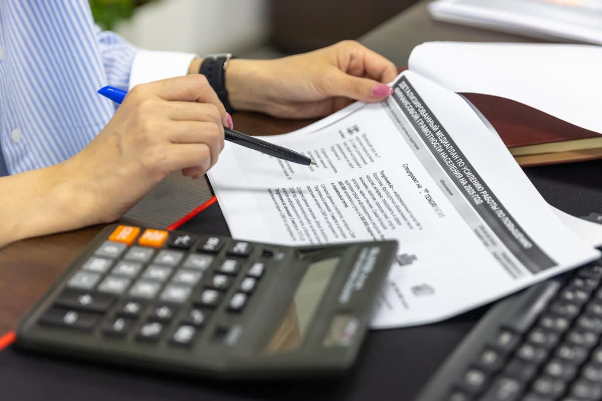 A close-up of hands holding a pen over papers, beside a calculator and keyboard: an illustrative image for finance and insurance.