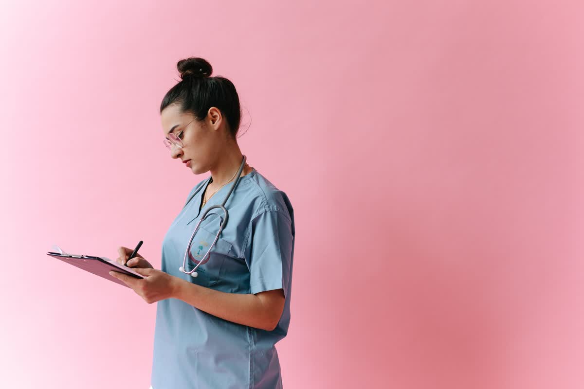A person in medical scrubs with a stethoscope writing on a clipboard: an illustrative image for healthcare and medical settings.