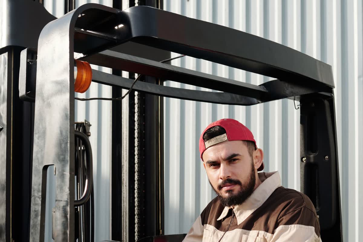 A person seated in a forklift cab in front of a corrugated warehouse wall: an illustrative image for transportation and logistics.