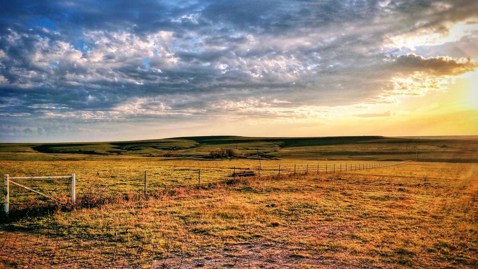 Open prairie and a fence line at sunrise in the Kansas Flint Hills: an illustrative image of the Great Plains, not a photograph of this place.